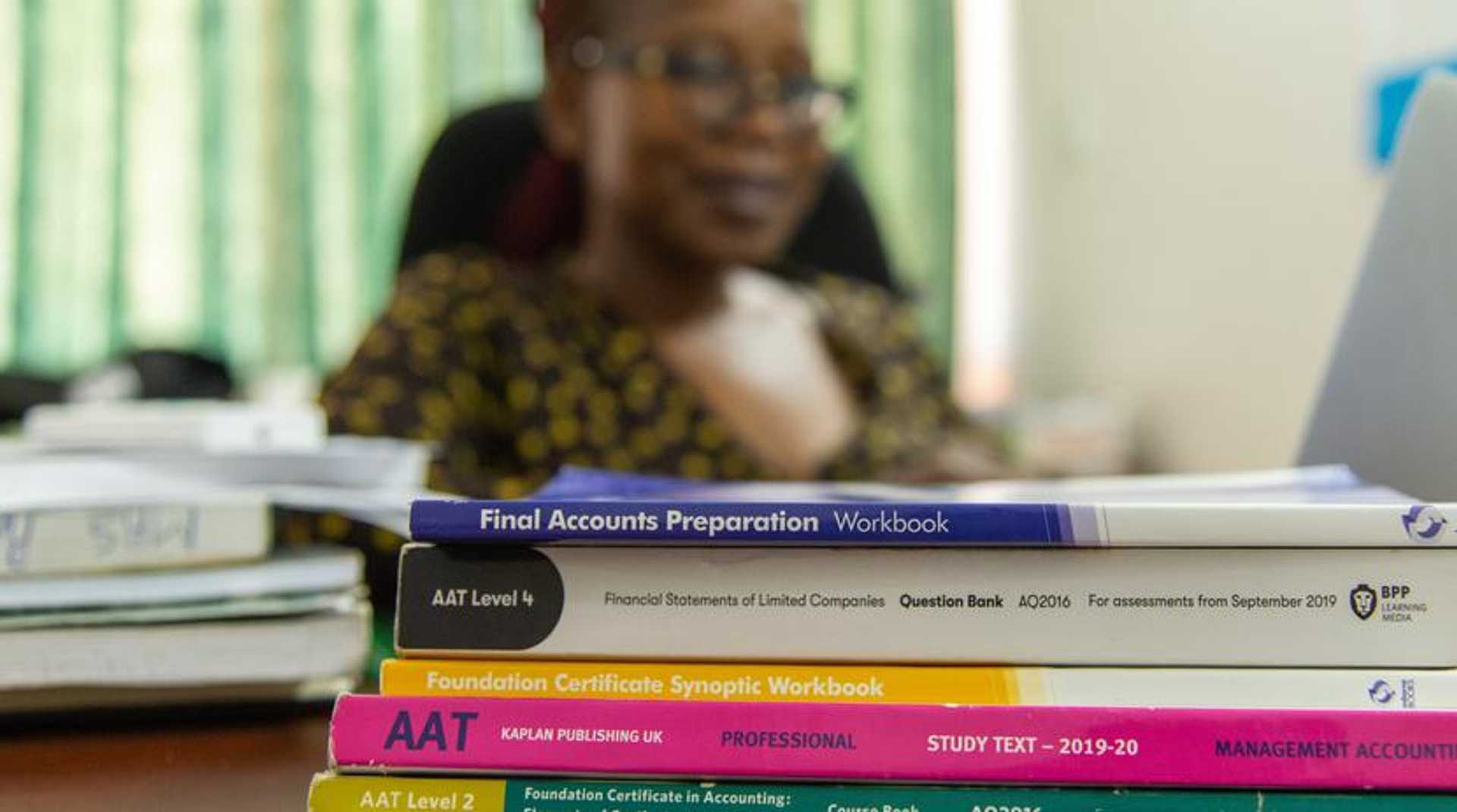 Margaret Dube, AAT tutor, behind a pile of AAT textbooks on a desk